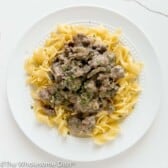 Ground beef stroganoff over egg noodles on a white plate.
