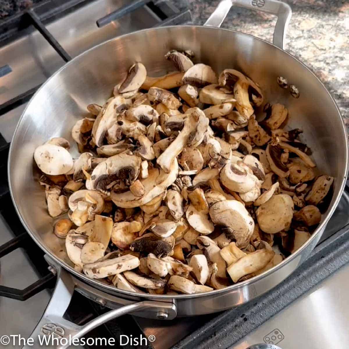 Mushrooms sautéing in a large skillet.