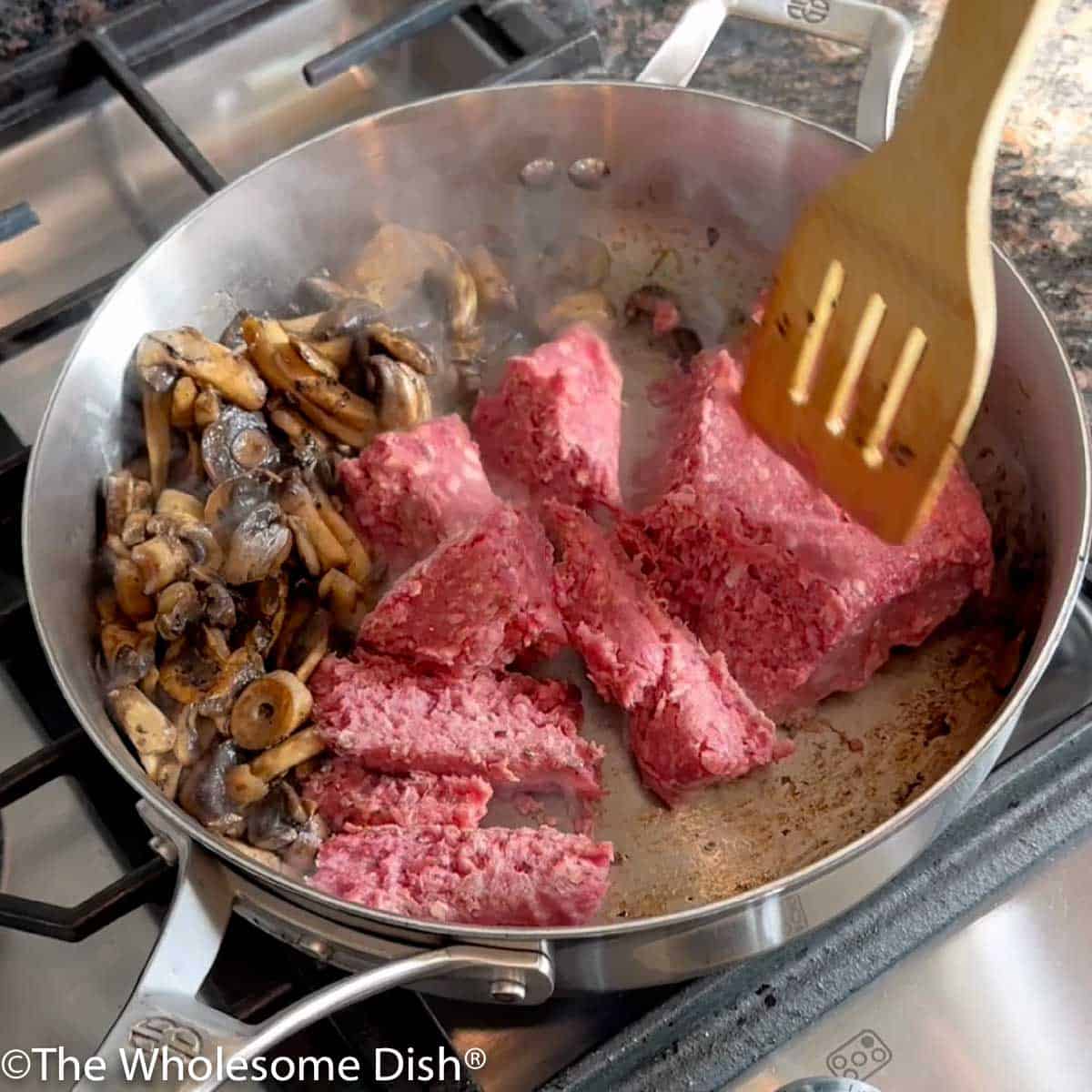 Ground beef being added to the mushrooms in the skillet.
