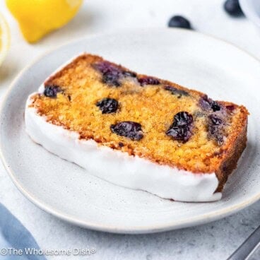 A slice of iced lemon blueberry bread on a white plate.
