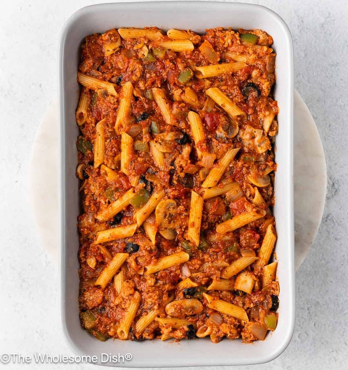 The pasta, sauce, and veggies in a casserole dish.