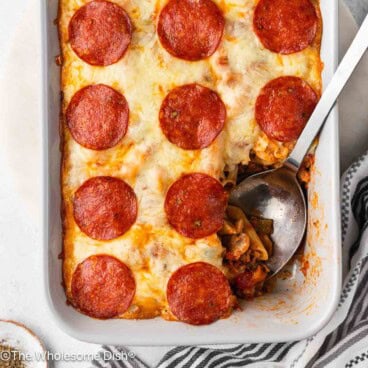 Casserole dish full of Supreme pizza pasta bake with a serving spoon.
