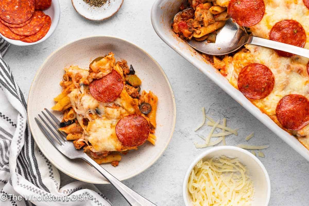 Plate full of Supreme Pizza Pasta Bake next to a casserole dish.