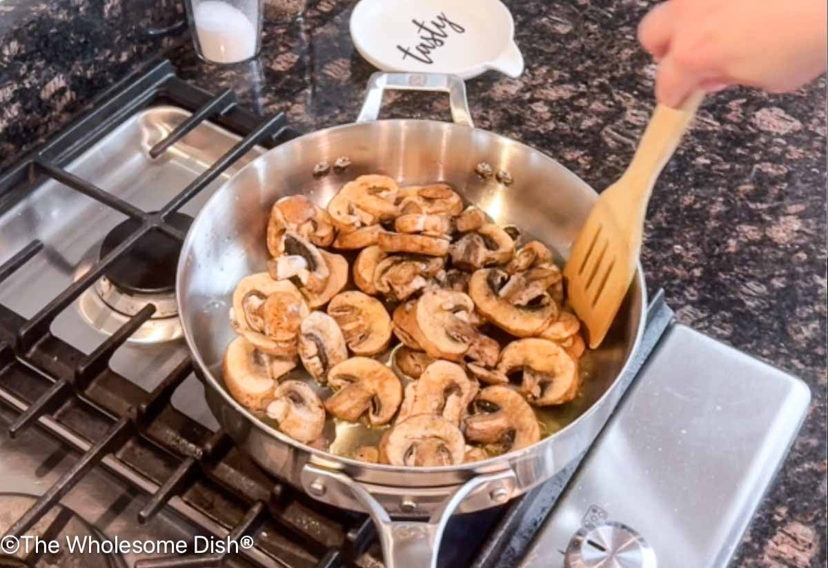 Sliced mushrooms sautéing in a skillet.