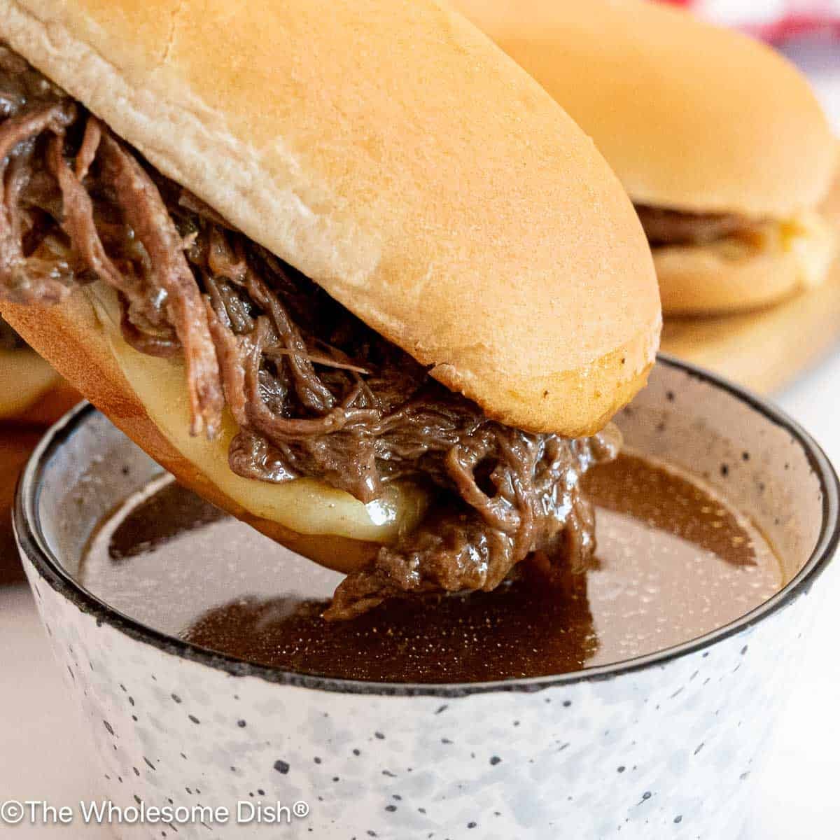 French dip sandwich being dipped into a small bowl of au jus sauce.
