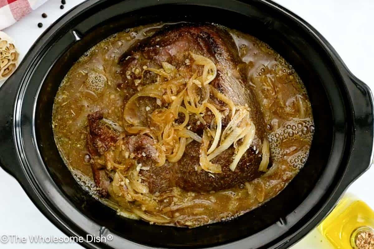 Crock Pot full of a chuck roast covered in beef broth and onions.
