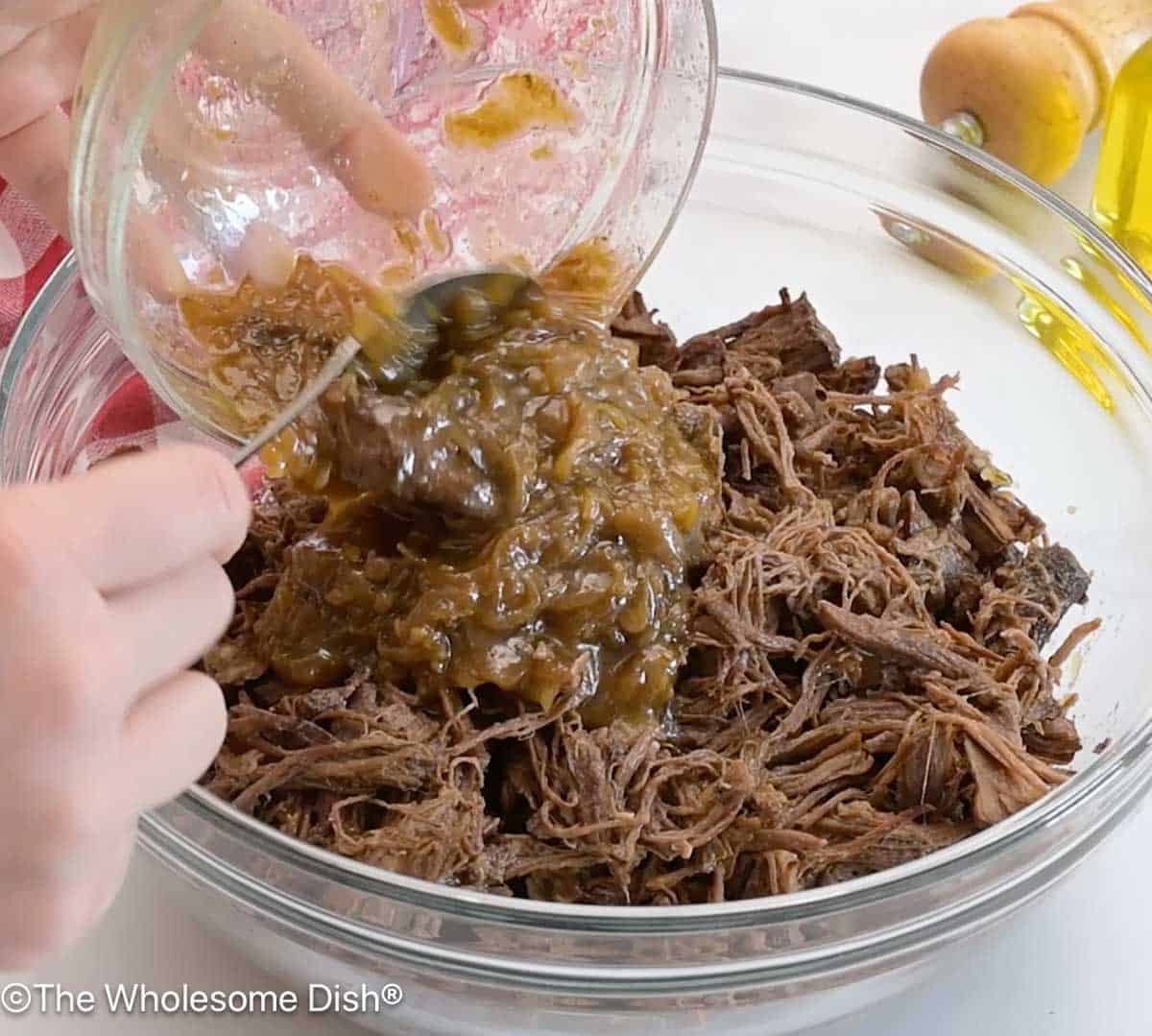 Bowl full of shredded beef with sautéed onions being added to it.