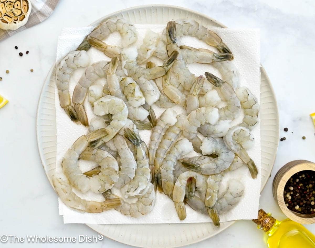 Raw shrimp on a paper towel lined plate.