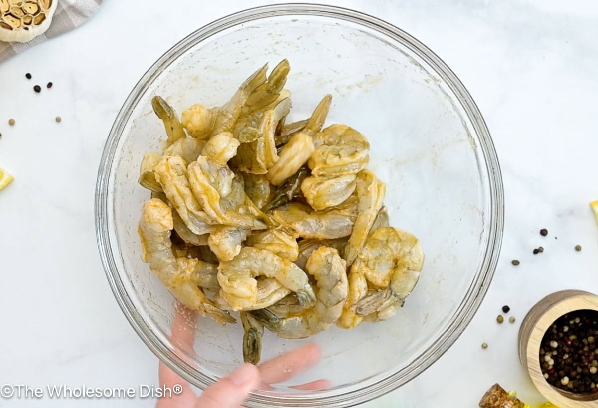 Mixing bowl full of uncooked shrimp coated in seasonings.