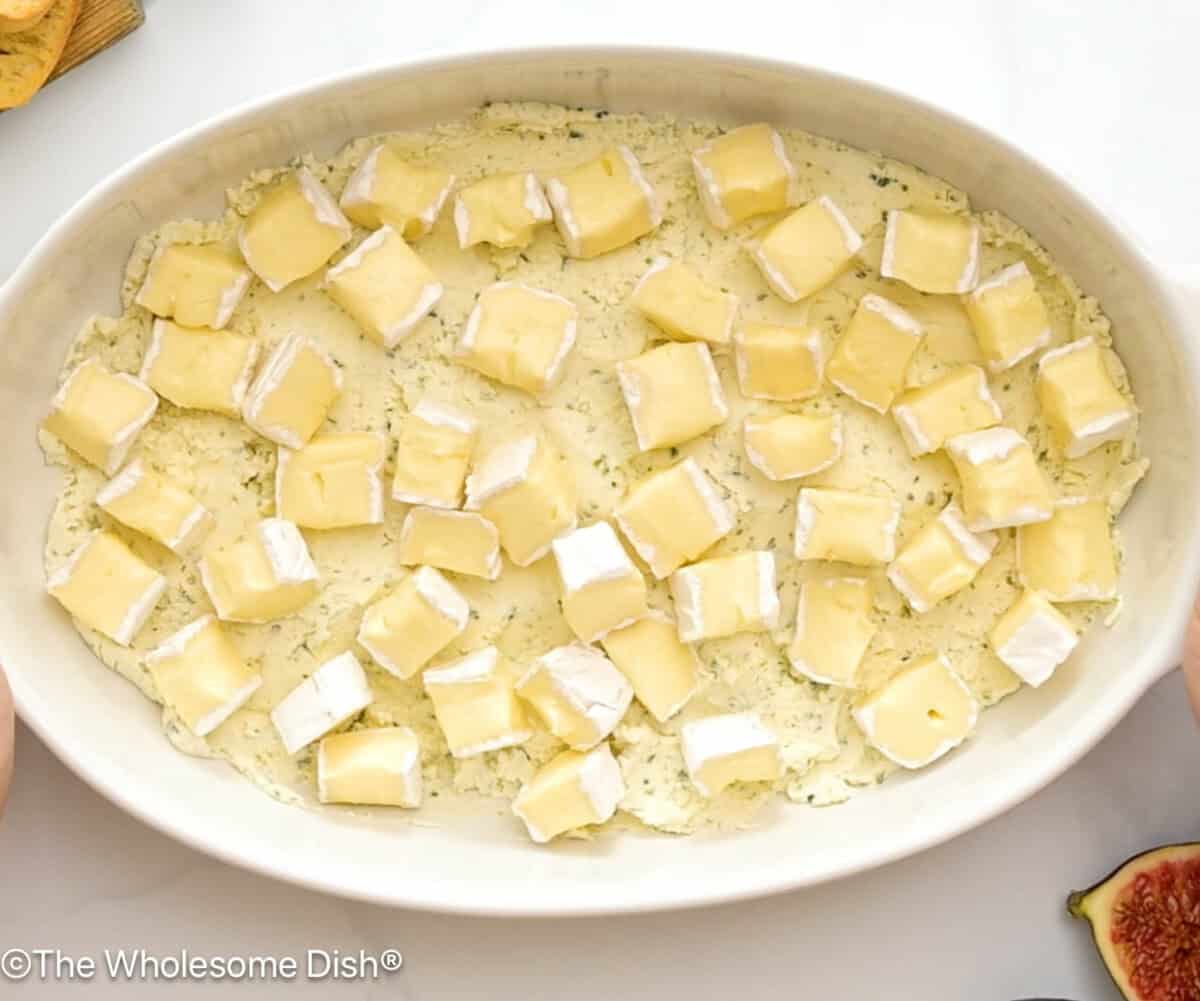 Boursin spread into the bottom a white casserole dish topped with chunks of Brie.